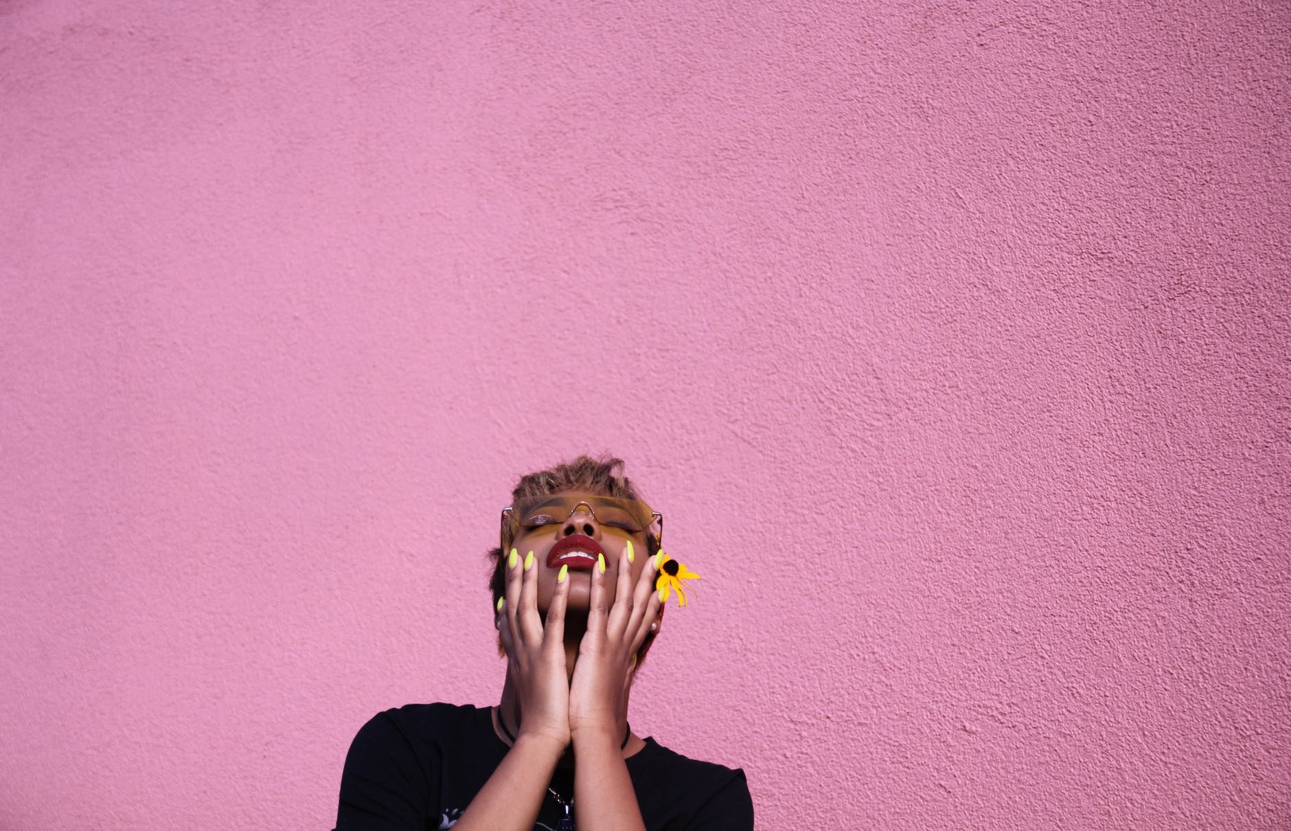 trendy young black woman touching face while throwing head back on pink background